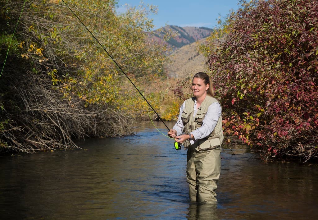 A woman fly fishing a river, casting from midstream
